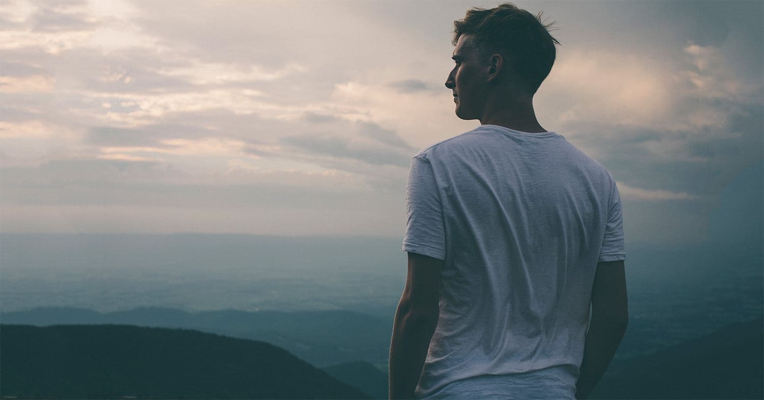 Man seen from behind in a blue shirt standing in a sunlit natural landscape