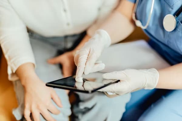 Clinician in gloves and scrubs showing a patient something on a tablet