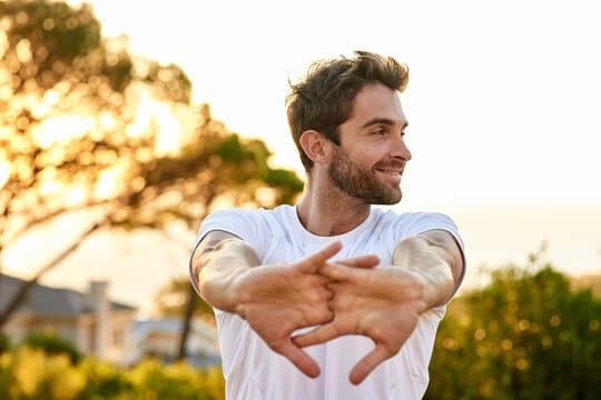Smiling bearded man stretching his arms in front of him outdoors at sunset