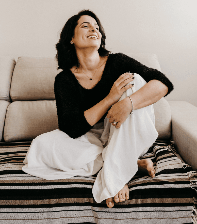 Smiling woman with dark hair relaxing on a sofa with her legs crossed