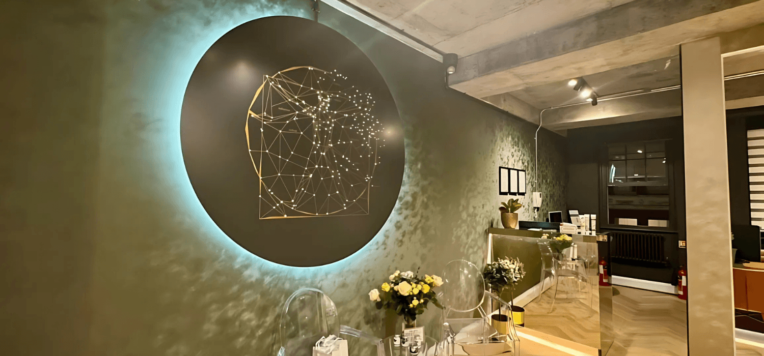 Clinic reception with a round illuminated wall panel showing a gold constellation figure, and a vase of yellow flowers